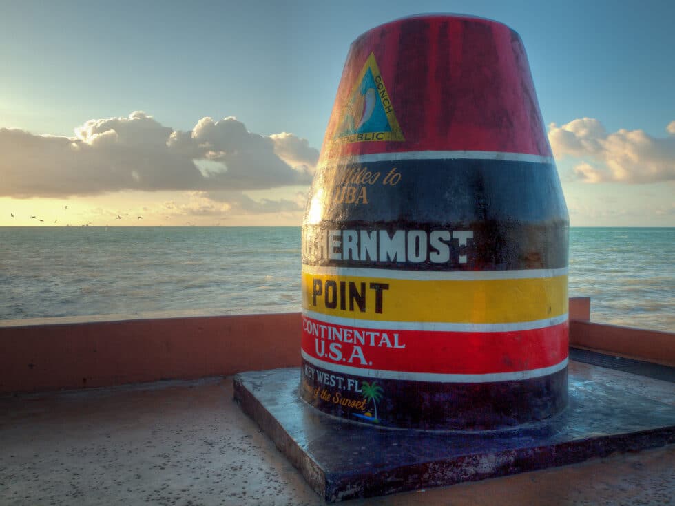 Vacation Travel Innovation image of the Southernmost Point marker in Key West beside the ocean.